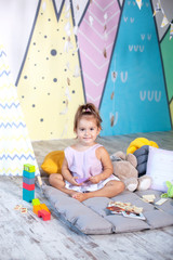 Baby girl plays a wigwam. Scandinavian interior and textiles for the nursery. Happy baby plays in a tent in a children's room. little girl plays in kindergarten. childhood concept, child development. 