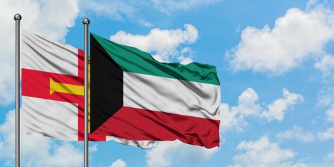 Guernsey and Kuwait flag waving in the wind against white cloudy blue sky together. Diplomacy...