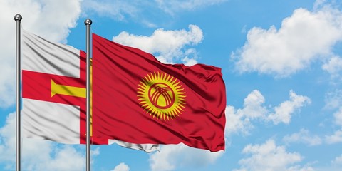 Guernsey and Kyrgyzstan flag waving in the wind against white cloudy blue sky together. Diplomacy concept, international relations.