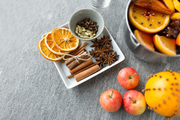christmas and seasonal drinks concept - pot with hot mulled wine, orange slices, aromatic spices and apples on grey background