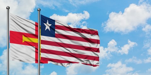 Guernsey and Liberia flag waving in the wind against white cloudy blue sky together. Diplomacy concept, international relations.