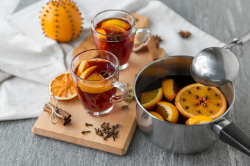 christmas and seasonal drinks concept - pot with hot mulled wine, orange slices, aromatic spices and ladle on grey background