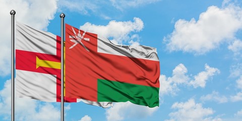 Guernsey and Oman flag waving in the wind against white cloudy blue sky together. Diplomacy concept, international relations.