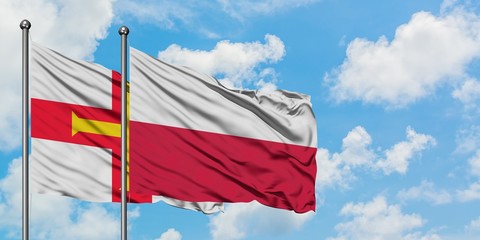 Guernsey and Poland flag waving in the wind against white cloudy blue sky together. Diplomacy concept, international relations.