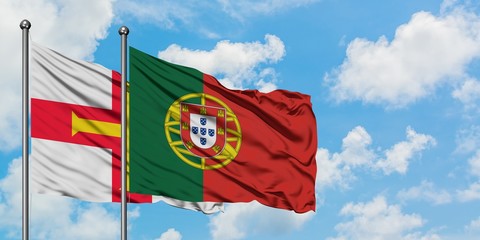 Guernsey and Portugal flag waving in the wind against white cloudy blue sky together. Diplomacy concept, international relations.