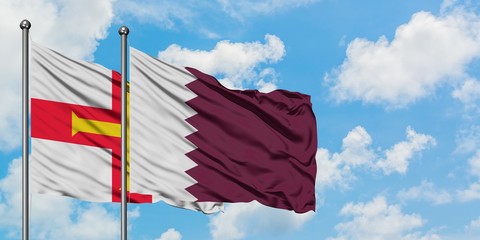 Guernsey and Qatar flag waving in the wind against white cloudy blue sky together. Diplomacy...