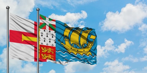 Guernsey and Saint Pierre And Miquelon flag waving in the wind against white cloudy blue sky together. Diplomacy concept, international relations.