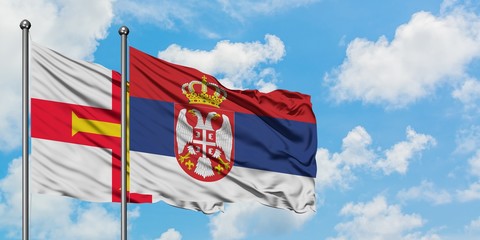 Guernsey and Serbia flag waving in the wind against white cloudy blue sky together. Diplomacy concept, international relations.