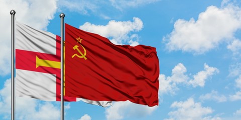 Guernsey and Soviet Union flag waving in the wind against white cloudy blue sky together. Diplomacy...