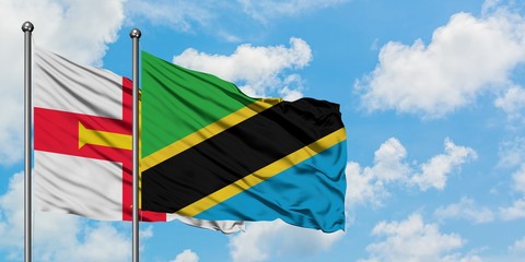 Guernsey and Tanzania flag waving in the wind against white cloudy blue sky together. Diplomacy concept, international relations.