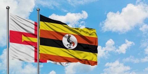 Guernsey and Uganda flag waving in the wind against white cloudy blue sky together. Diplomacy concept, international relations.