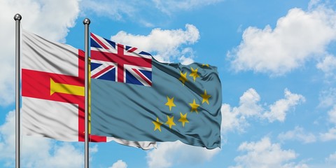 Guernsey and Tuvalu flag waving in the wind against white cloudy blue sky together. Diplomacy...