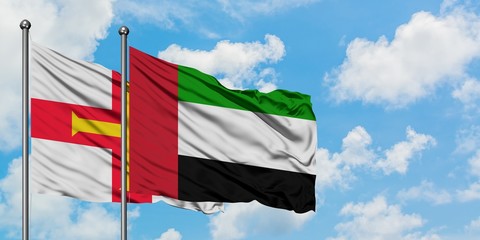 Guernsey and United Arab Emirates flag waving in the wind against white cloudy blue sky together. Diplomacy concept, international relations.