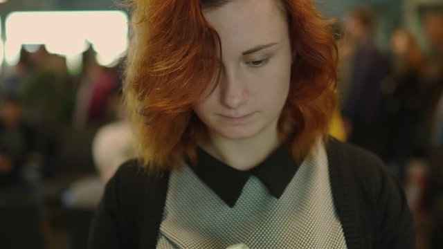 Sad redhead woman in an airport queue missed her flight - Eye contact and blurry background with people walking in the back