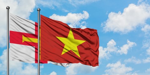 Guernsey and Vietnam flag waving in the wind against white cloudy blue sky together. Diplomacy concept, international relations.