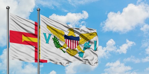 Guernsey and United States Virgin Islands flag waving in the wind against white cloudy blue sky...