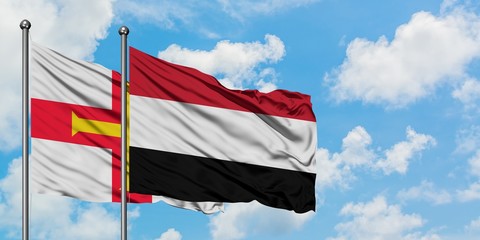 Guernsey and Yemen flag waving in the wind against white cloudy blue sky together. Diplomacy...