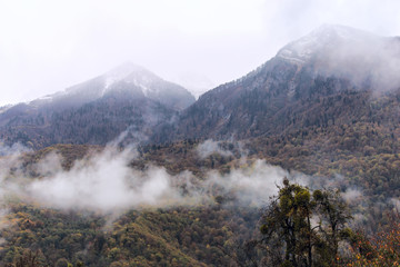 Fog in the mountains against the background of peaks with snow in the fall in Sochi, Russia.