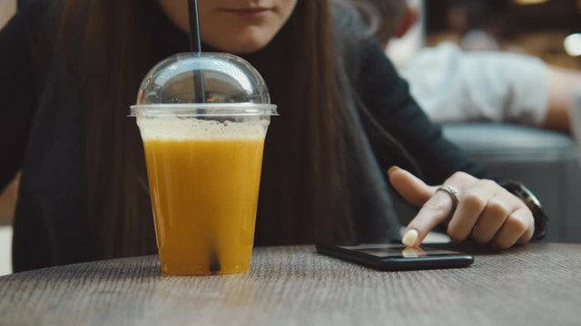 Young woman browsing on smartphone in cafe on wooden table, drinking juce. Businesswoman typing on mobile phone. 4K UHD