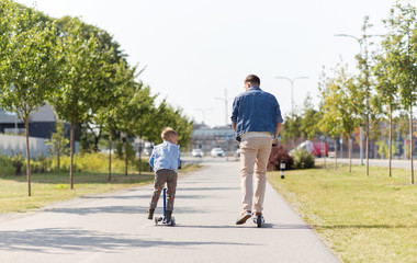 Fototapeta premium family, leisure and fatherhood concept - happy father spending time with little son riding scooter in city