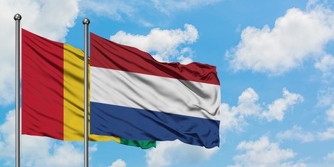 Guinea and Netherlands flag waving in the wind against white cloudy blue sky together. Diplomacy concept, international relations.