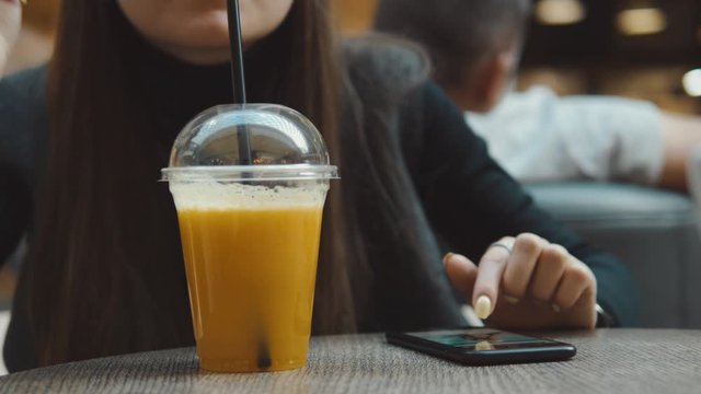 Young woman browsing on smartphone in cafe on wooden table, drinking juce. Businesswoman typing on mobile phone. 4K UHD