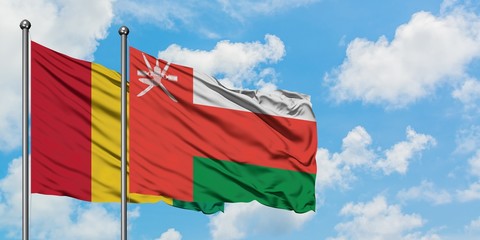 Guinea and Oman flag waving in the wind against white cloudy blue sky together. Diplomacy concept, international relations.