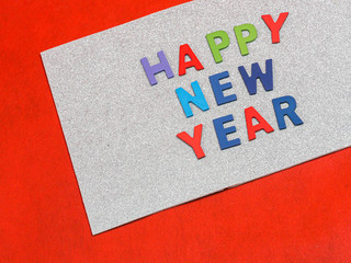 Top view or directly above of multicolored wooden alphabet of happy new year text on rough gradient glitter white paper texture and vivid or vibrant red background.Greeting card for new year holidays.