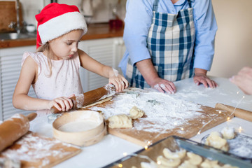 Obraz na płótnie Canvas Family is cooking Christmas cookies together in cozy home kitchen for dinner. Kid and grandmother are preparing holiday food. Little girl helps senior woman. Lifestyle moment. Children chef concept.