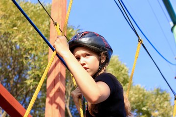 Girl in safety equipment hiking in the rope park . Сlimbing adventure park.