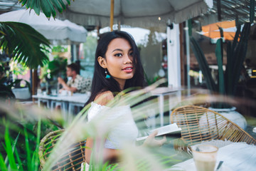 Stylish casual Asian woman reading book in street cafe