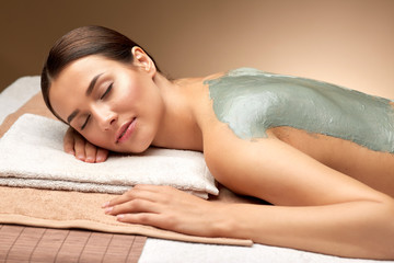 wellness, beauty and cosmetology concept - beautiful young woman lying with blue clay mask on back at spa