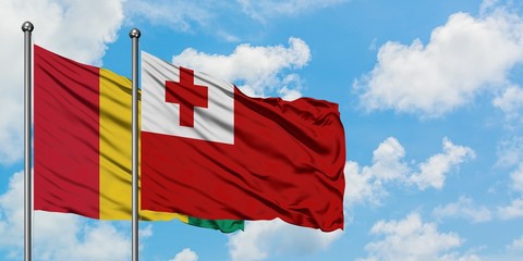 Guinea and Tonga flag waving in the wind against white cloudy blue sky together. Diplomacy concept, international relations.