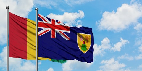 Guinea and Turks And Caicos Islands flag waving in the wind against white cloudy blue sky together. Diplomacy concept, international relations.