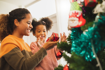 Black african mother and her cute daughter decorating christmas tree for christmas and happy new...