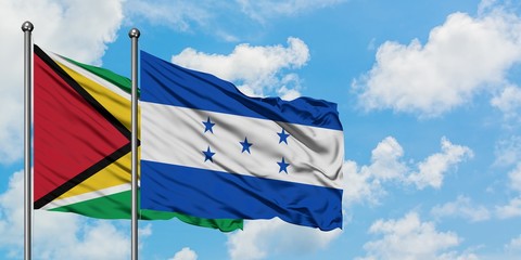 Guyana and Honduras flag waving in the wind against white cloudy blue sky together. Diplomacy...