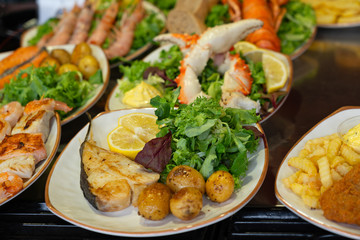 Sea food fish mix plates with lemon, vegetables, crab legs and green salad.