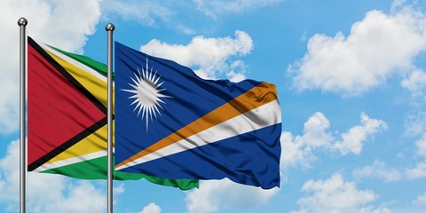 Guyana and Marshall Islands flag waving in the wind against white cloudy blue sky together. Diplomacy concept, international relations.