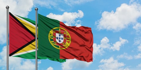 Guyana and Portugal flag waving in the wind against white cloudy blue sky together. Diplomacy concept, international relations.
