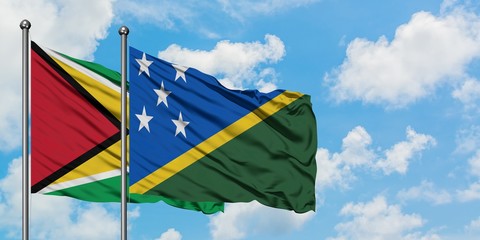Guyana and Solomon Islands flag waving in the wind against white cloudy blue sky together. Diplomacy concept, international relations.