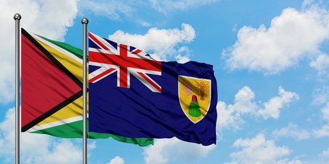 Guyana and Turks And Caicos Islands flag waving in the wind against white cloudy blue sky together. Diplomacy concept, international relations.