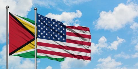 Guyana and United States flag waving in the wind against white cloudy blue sky together. Diplomacy concept, international relations.