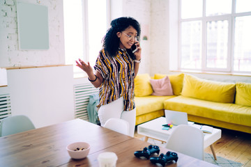Sad black woman speaking on phone while standing in living room - Powered by Adobe