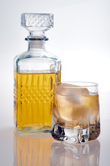 Bottle and glass of whiskey with ice on a white background with reflection. Isolated and frontal view