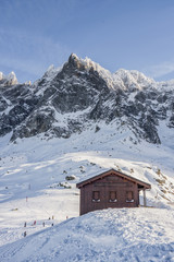 Fototapeta na wymiar Dark wooden house on snow slope before Aiguille du Plan
