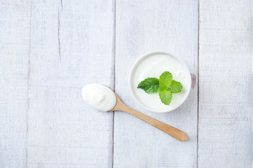 Natural white yogurt with mint leaf on white cup with wooden spoon on white wooden table.Top view.