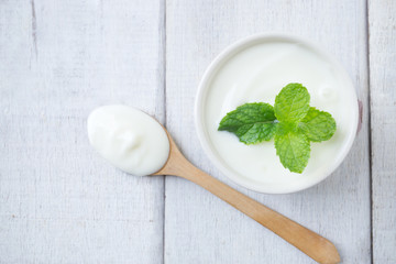 White yogurt with mint leaf on white cup with wooden spoon on white wooden table.Top view.