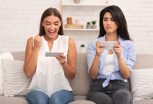 Girl being envious her friend's victory in mobile game indoor