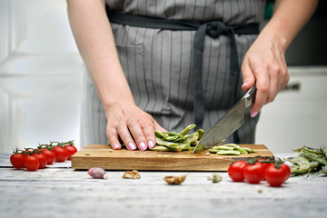 The chef prepares green beans, tomatoes on a branch, red onions in the white kitchen. wooden cutting Board on rustic background