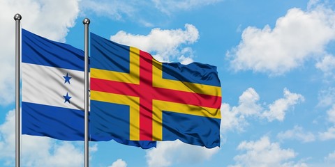 Honduras and Aland Islands flag waving in the wind against white cloudy blue sky together....